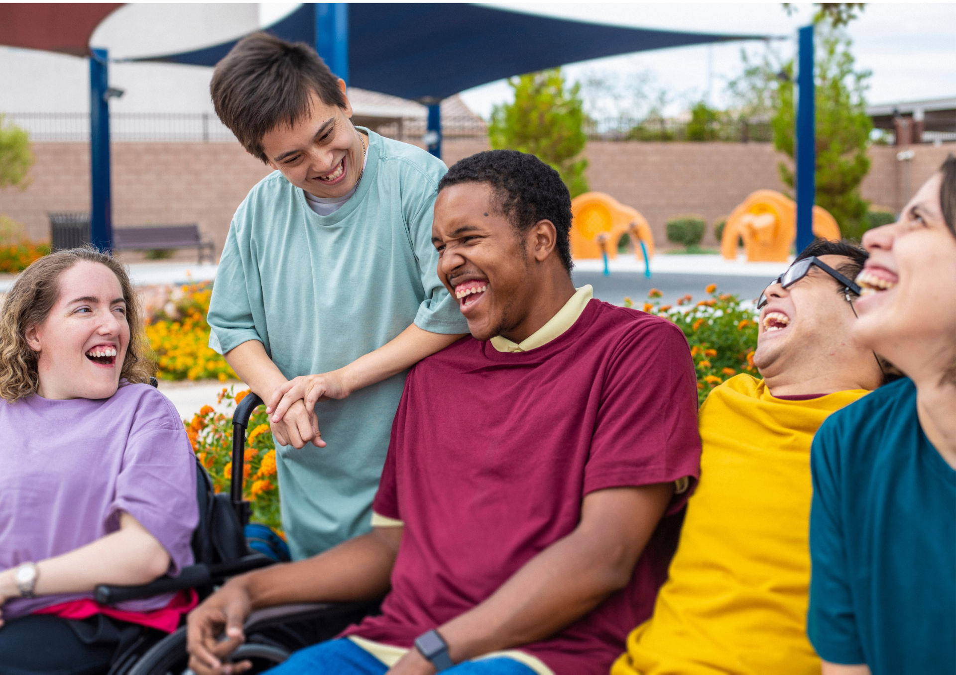 A diverse group of adults with IDD laughing together outdoors in a supportive community setting